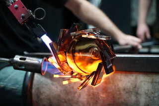 A close up of a gaffer creating an amber glass cup with square pieces of glass around the lip of the cup